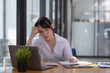 © amnaj - Young Asian woman feeling migraine head strain. Tired, Overworked businesswoman financier while working on laptop computer in office.