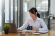 © amnaj - Smiling young happy Asian businesswoman working with laptop and documents in office. Accountant or beautiful asian female worker working happily in the office...