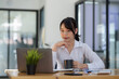 © amnaj - Smiling young happy Asian businesswoman working with laptop and documents in office. Accountant or beautiful asian female worker working happily in the office...