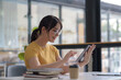 © amnaj - Casual City Lifestyle. Asian Woman Enjoying Coffee and Browsing on Tablet at Cafe.