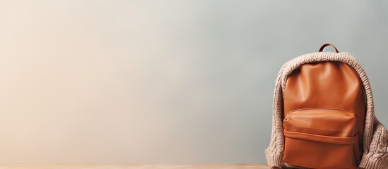 Poster - Black backpack paired with a brown knitted sweater viewed from behind against a isolated pastel background Copy space