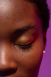 © wavebreak3 - Close up of closed eye of african american woman with short hair on purple background
