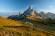 Sunrise at Passo Giau with road and parked cars and campers with sun shining at meadow and peaks in  the background during summer morning in august and grass in foreground