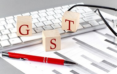 Wall Mural - GST written on a wooden cube on the keyboard with chart on grey background