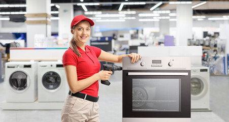 Poster - Repair woman with a drill standing next to an oven