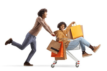 Poster - Caucasian guy pushing an african american friend with shopping bags inside a shopping cart