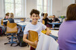 © Maskot - Portrait of happy schoolboy sitting on chair at desk in classroom