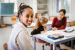 © Maskot - Side view portrait of smiling female student sitting in classroom