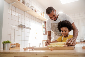 Portrait of African American dad little son having fun in kitchen home, baking pastry in modern kitchen together, kneading Dough prepare cookie pizza. Love fun make homemade food hobby or leisure time