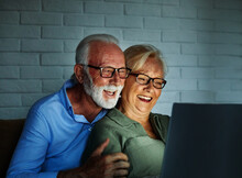 television watching couple laptop night computer home evening elderly senior mature active old woman man movie entertainment fun love together glowing screen