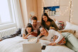 © Maskot - Cheerful multiracial friends watching movie together on laptop at home