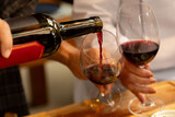 Fototapeta  - Close em garrafa de vinho tinto sendo servido em duas taças seguradas por casal em fundo desfocado.