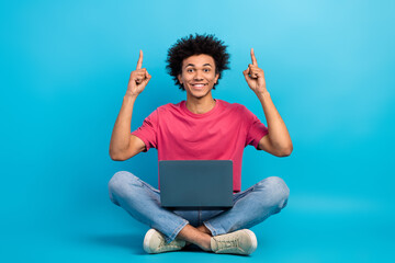 Full size photo of attractive young man netbook fingers point up empty space dressed stylish pink clothes isolated on blue color background
