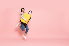 Asian Happy Woman Jumping With Yellow Suitcase Isolated On Pink Background, Tourist Girl Having Cheerful Holiday Trip Concept