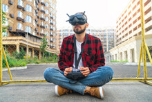 Pilot Man Sitting On The Street Road Using Goggles And Remote Controller To Operate Generic Design Fpv Drone For Aerial Urban Photography And Videography
