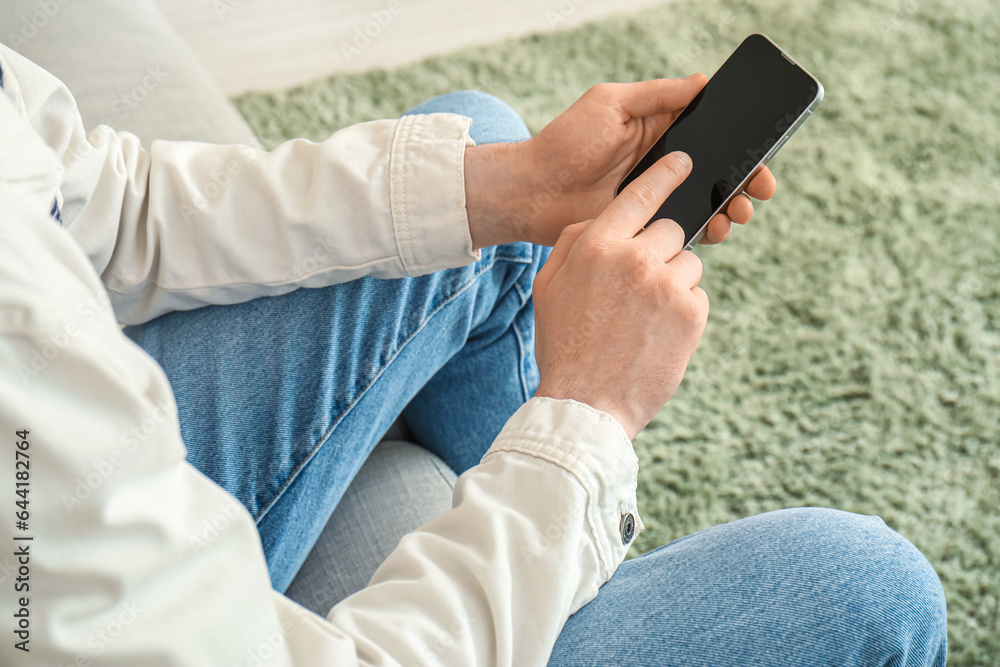 Young man with mobile phone messaging at home, closeup