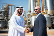 © Jasmina - Arab man in keffiyeh shake hands with a white business man after a successful business deal. Oil refinery in the background