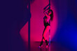 Girl pole dancer in the gym with neon light. Sports pole dancing horizontal photo with motion blur effect.