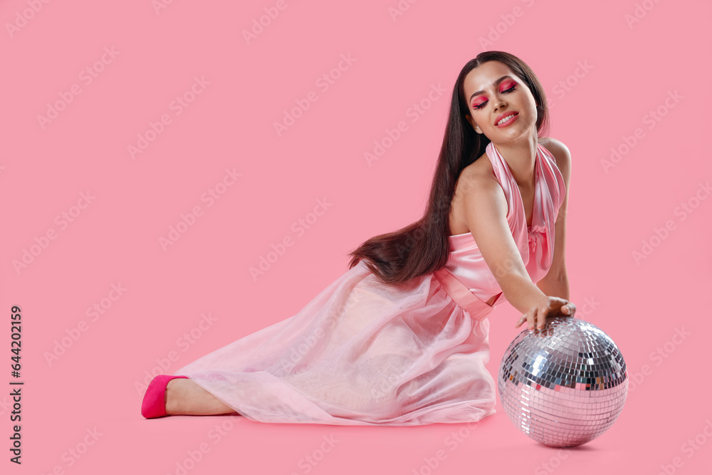 Stylish young woman with disco ball on pink background