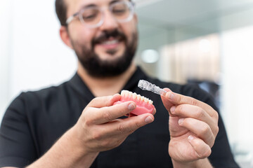Aufkleber - Cheerful dentist showing clear aligners on artificial human jaw presenting innovative teeth correction in stomatology clinic specialist holding medical device closeup