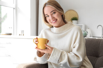 Sticker - Young woman with cup of hot tea sitting in kitchen