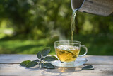 Pouring hot water in a glass cup with sage leaves, healthy herbal tea and home remedy for coughs, sore throat and digestive problems, dark green background, copy space
