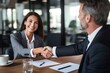 © yj - Happy professional mature Latin businessman and businesswoman wearing suits shake hands sitting at table having partnership business contract agreement. generative AI