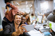 © Geber86 - Diverse group of coworkers taking a selfie on a smartphone in the office of a startup company