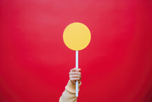 Person Is Holding Yellow Sign Mockup In Front Of Vibrant Red Background. This Image Can Be Used To Represent Sweetness, Joy, Or Fun And Playful Atmosphere.