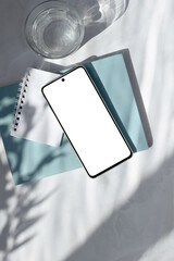 Wall Mural - Smartphone empty screen mock up, blue notebook, glass with water on white table with natural sunlight shadows. Aesthetic business brand template, copy space