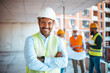 © Dragana Gordic - Portrait of satisfied construction site manager wearing safety vest and white helmet at construction site. Young architect watching construction site with confidence looking at camera.