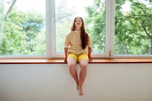 Teenage Girl With Down Syndrome Sitting On Window Sill At Home