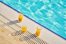 Glasses Of Orange Juice Near Swimming Pool On Sunny Day