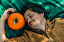 Smiling Man Lying Near Pumpkin On Green Blanket