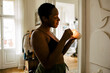 © Maskot - Side view of smiling young woman holding lit candle at home
