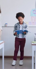 Wall Mural - Child, boy reading and classroom with kid speaker, book and education at a school. Students, learning and notebook with development, knowledge and study work with story presentation of youth speech