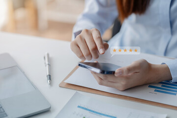 Asian woman holding a smartphone, she rates store reviews and places online shopping orders. Giving stars to stores is a review for making decisions about using the service. Service rating concept.