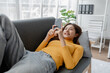 © PHOTO4U - Asian woman is in the living room and uses social media on a smartphone. Female company employee on vacation. Using vacation time and free time to relax at home. Weekend vacation day doing activities.