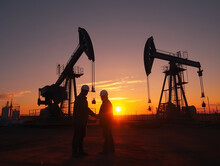 Silhouette Of Two Engineers Handshaking And Making Corporate Contract Outside In Front Of Oil Pump. People In Helmets Working In Field At The Oil.