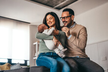 Portrait Of Young Happy Man And Woman Holding Newborn Cute Babe Dressed In White Unisex Clothing.