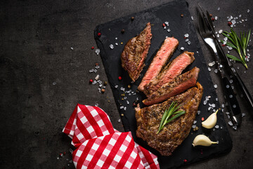 Wall Mural - Beef steak on black. Grilled beef steak striploin medium rare on slate serving board. Top view with copy space.