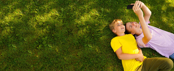 Two happy broters lying on green grass in meadow with cellphone. children looking at mobile phone screen outside