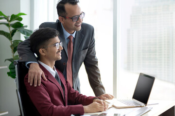 Indian businessman father and son smiling at desk, businessman father is proud to have his son help him at the company, side view