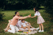 © Roman - Cheerful family sitting on the grass during a picnic in a park, there is a basket with meal and toys for the kids