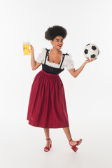 Wall Mural - african american oktoberfest waitress with mug of foamy beer playing football on white, full length