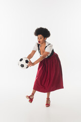 Wall Mural - african american oktoberfest waitress in traditional bavarian dirndl playing football on white