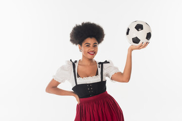 Wall Mural - smiling african american bavarian waitress in dirndl with soccer ball on white, oktoberfest concept