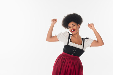 Wall Mural - excited african american waitress in traditional bavarian costume rejoicing and gesturing on white