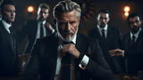 Fototapeta Most -  The most interesting man in the world. Middle aged classic beard gentleman wearing expensive suit and accessories, standing in a dark place, with his team in his background. Serious mafia boss 