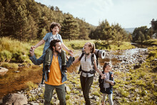 Young Family Crossing A Creek While Hiking In The Forest And Mountains